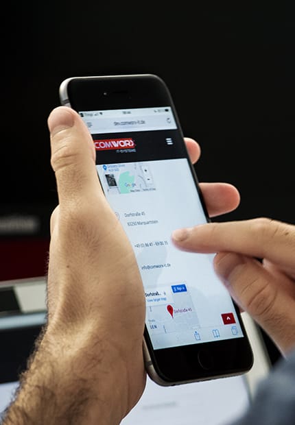 Hand hält Smartphone mit geöffneter COMWORX IT Website – Kontaktinformationen und Standortanzeige für IT-Dienstleistungen